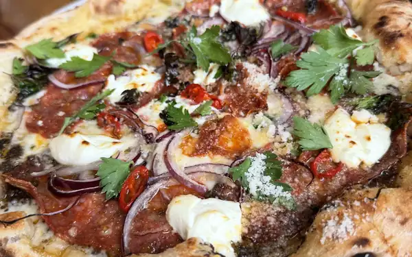 Pizza z szynką, mozzarellą i pomidorkami na drewnianym stole